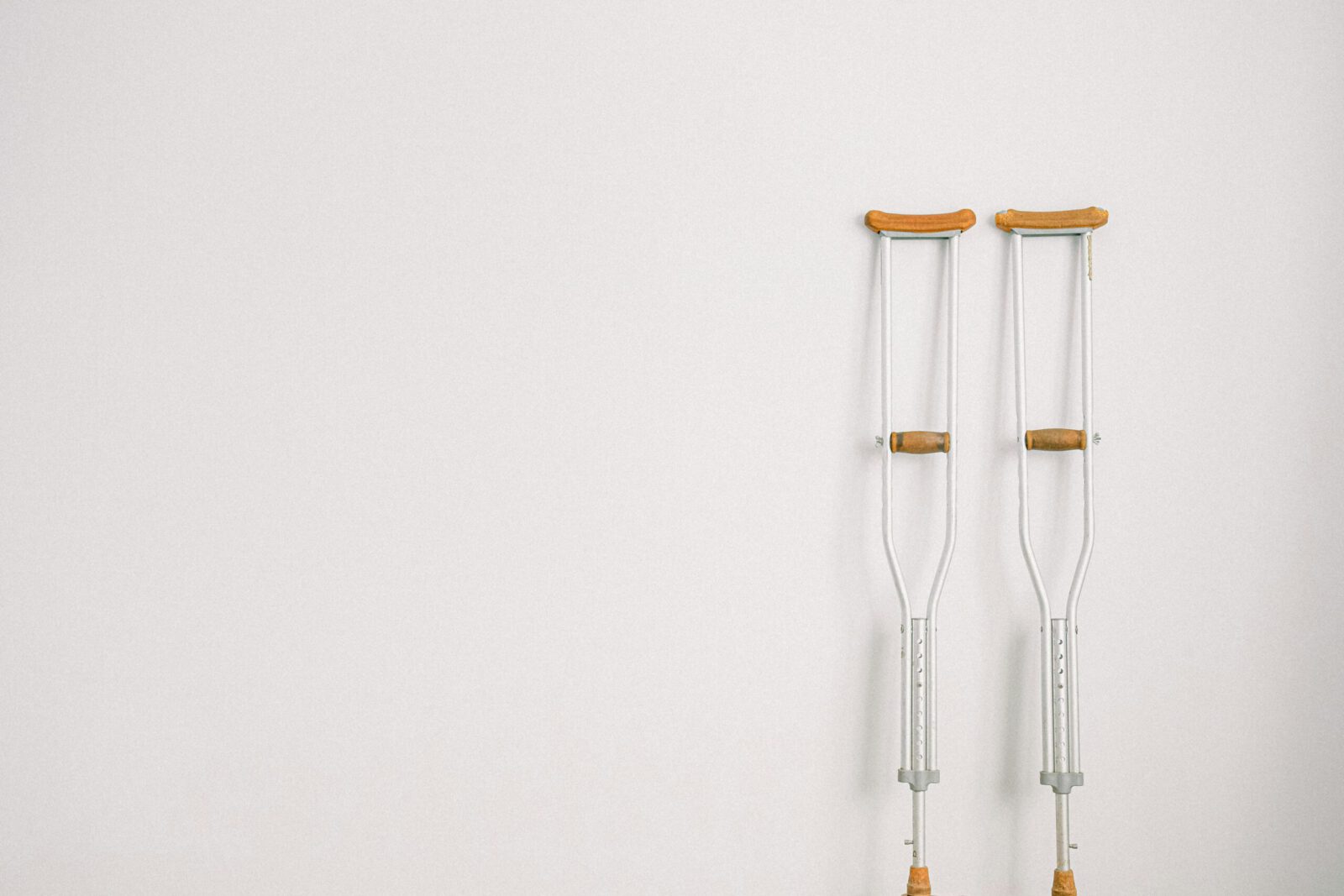 Minimalist image of a pair of crutches leaning on a white wall, symbolizing mobility aid.